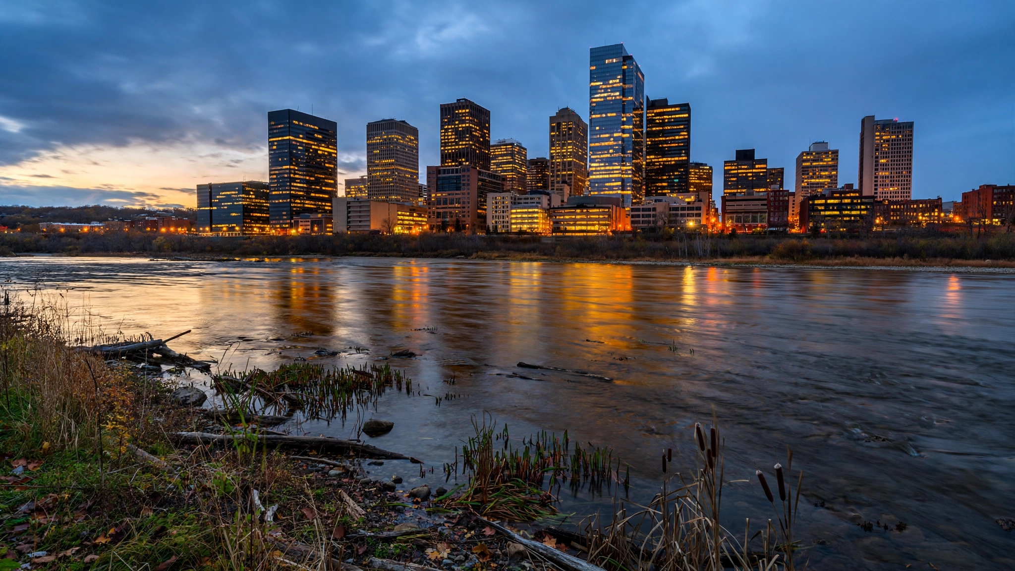 A Midwestern city downtown skyline at dusk with a river in the foreground