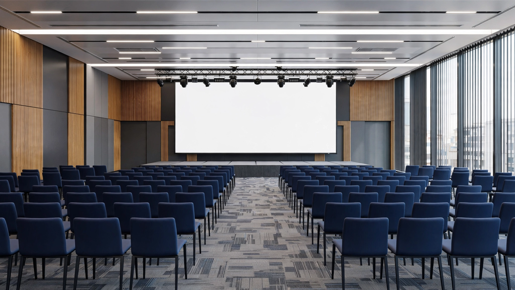 An empty modern conference hall with rows of blue chairs facing a large blank stage screen.