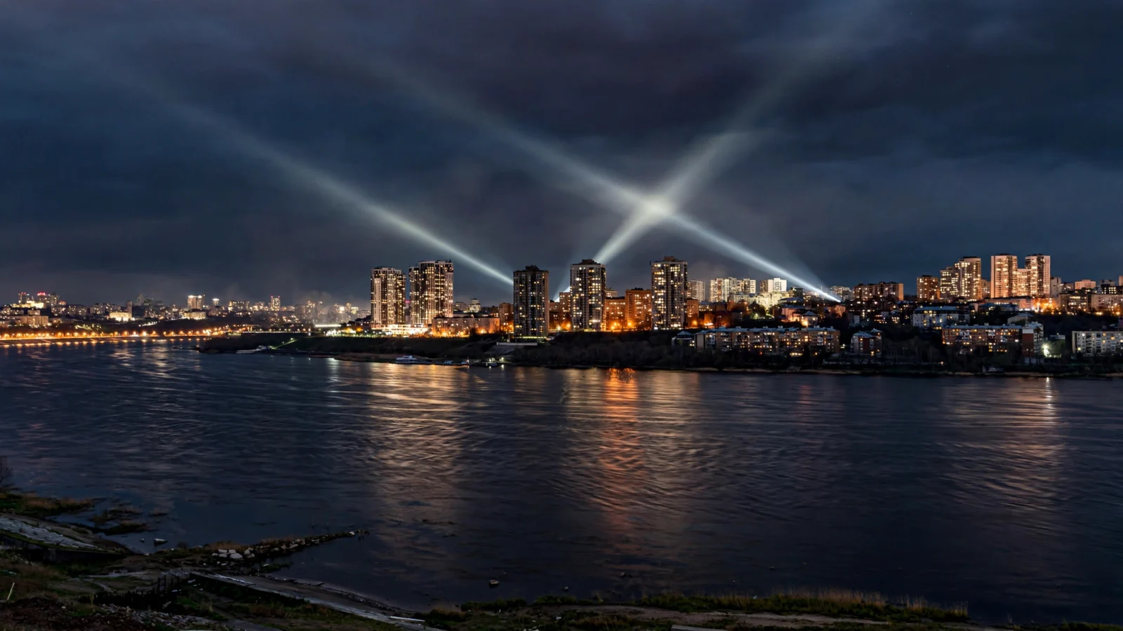 A nighttime view of Kyiv's skyline with searchlight beams in the sky above the river