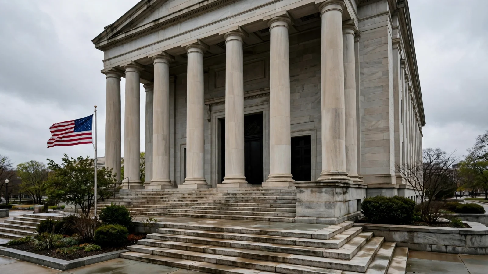 Stone columns and steps of a federal courthouse with an American flag flying beside the entrance under an overcast sky