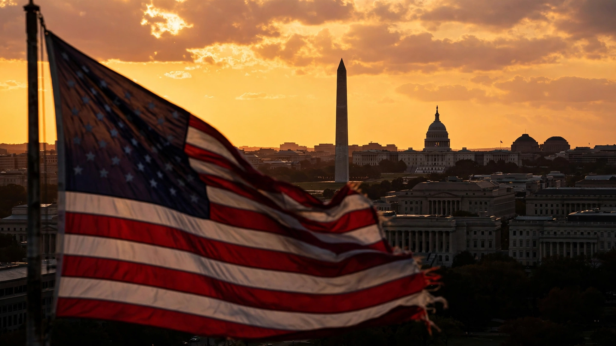American flag waving in the foreground with the Washington Monument and US Capitol at sunset in the background